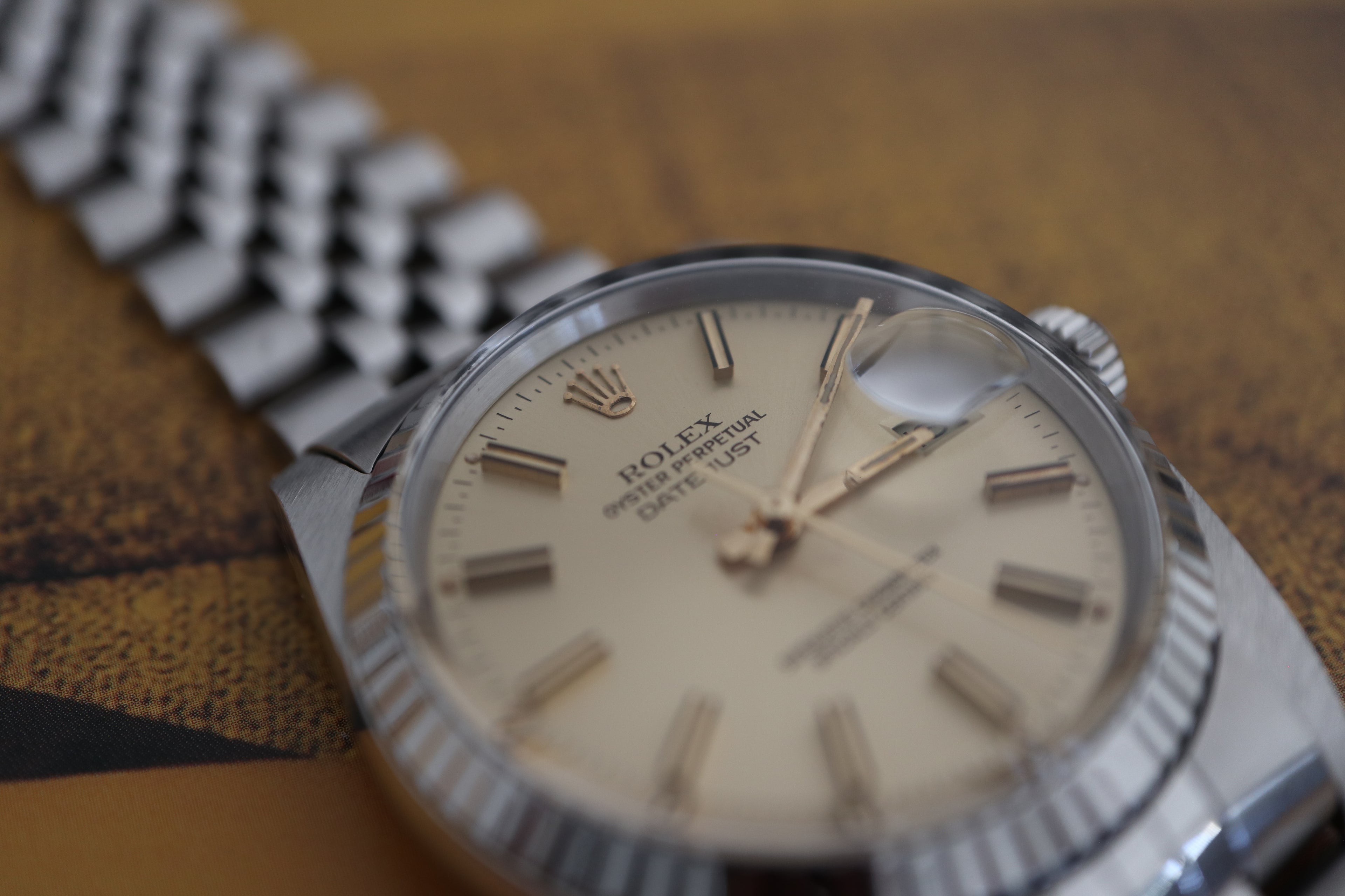 Close-up of Rolex Datejust with champagne dial, fluted bezel, and jubilee bracelet photographed on a warm textured background.