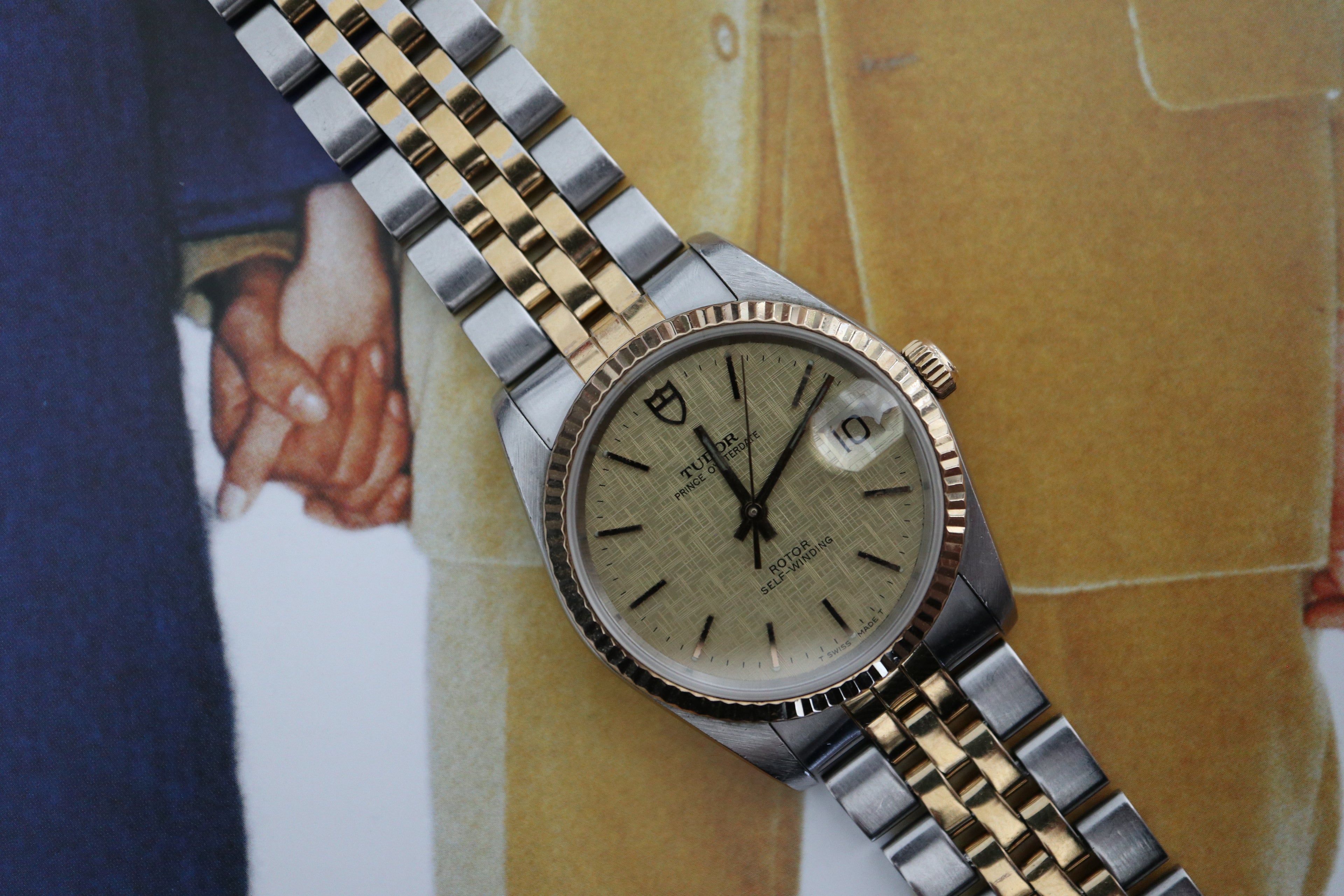 Two-tone Tudor Prince Oysterdate watch with champagne linen dial and jubilee bracelet photographed on a vintage magazine background.